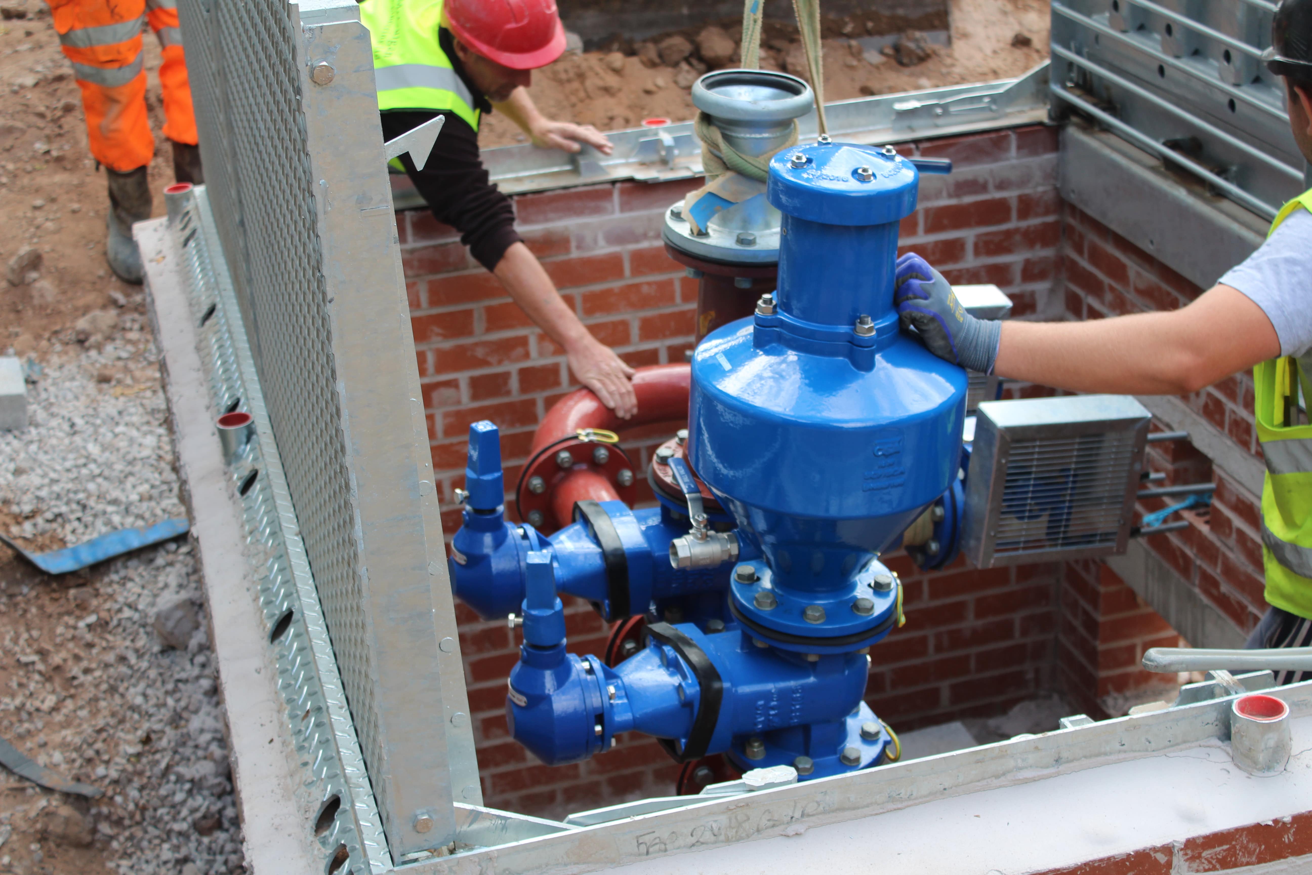 Two service engineers installing a blue T-T pump in the ground as part of a pumping station installation.