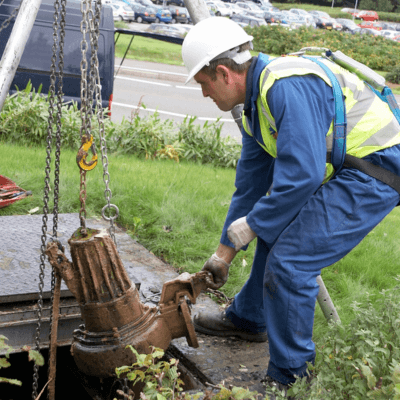 A T-T Engineer in a yellow high visibility jacket removing a sewage pump from the ground on-site.