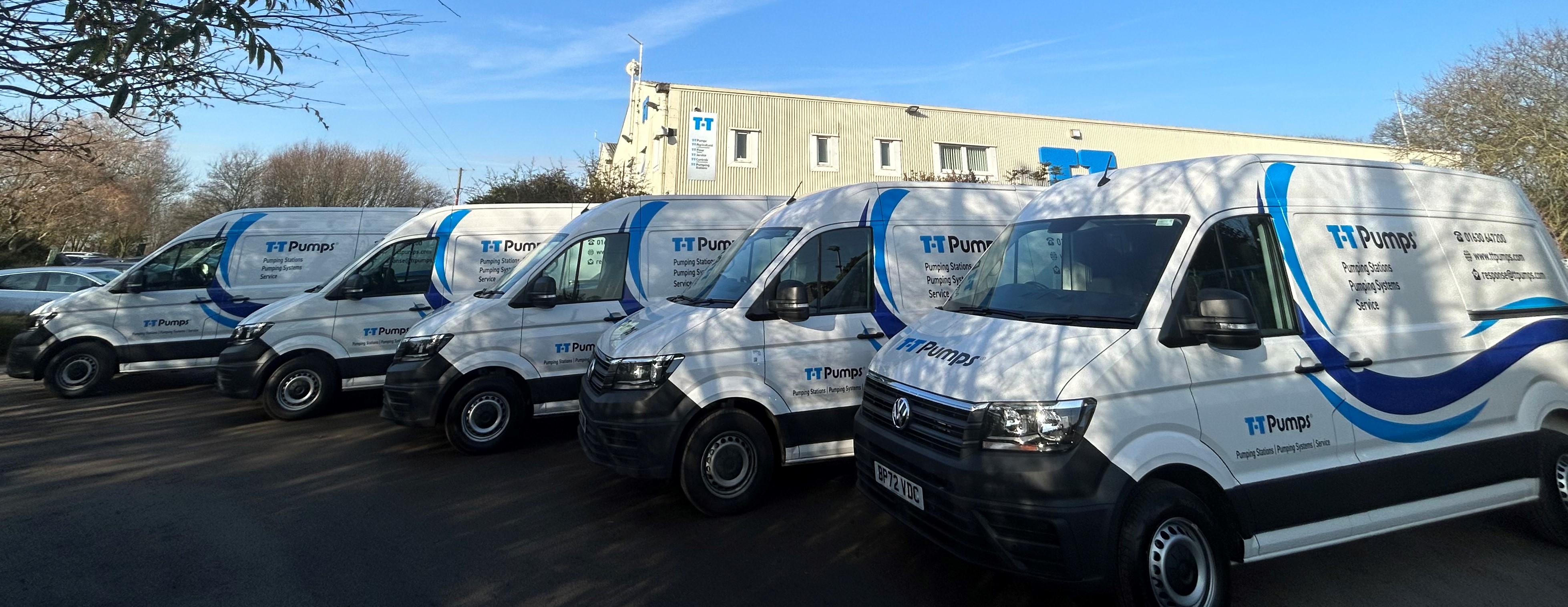 Five T-T Service vans parked in front of the T-T Headquarters, listing Pumping Stations, Pump Spares and Service on the side of the vans.