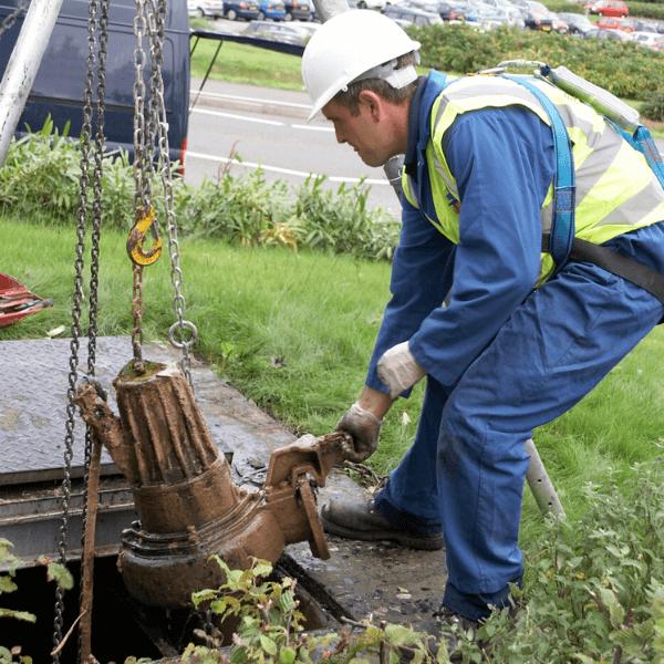 A T-T Service engineer removing a submersible pump from the ground on-site, wearing a high visibility vest.