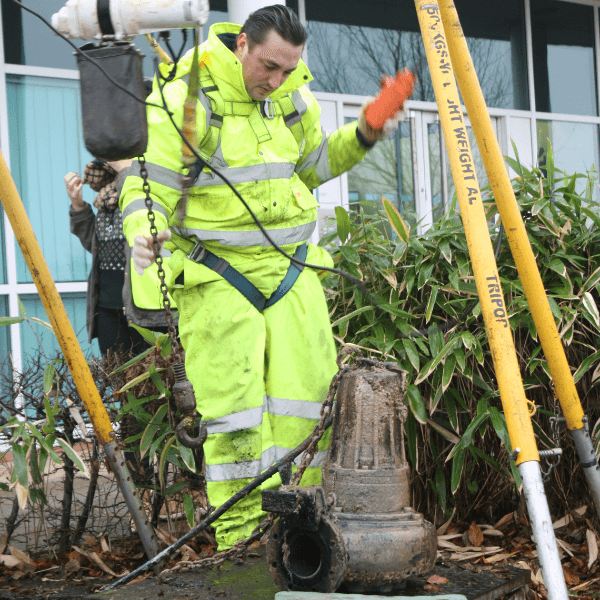 A T-T Service engineer removing a submersible pump from the ground on-site, wearing a high visibility suit.