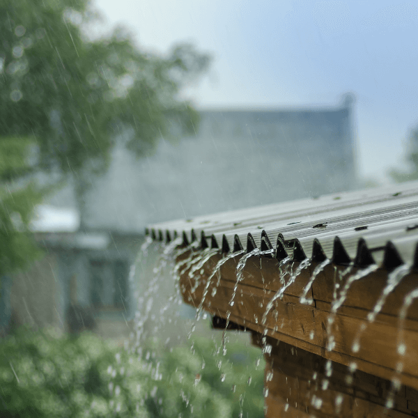 A photograph of rainwater running off the edge of a rooftop, the sky is grey in the background.